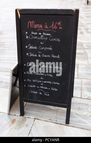 Eine Restaurantmenü-Tafel mit französischen Gerichten, die mit Kreide auf einem Straßenpflaster in Bastia, Korsika, Frankreich geschrieben sind. Stockfoto