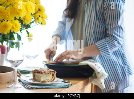 Abendessen für die Familie. Frau, die Portionen von Lebensmitteln. Serviert Tisch. Gelbe Blumen auf dem Tisch. Tisch in der Nähe des Fensters. Stockfoto