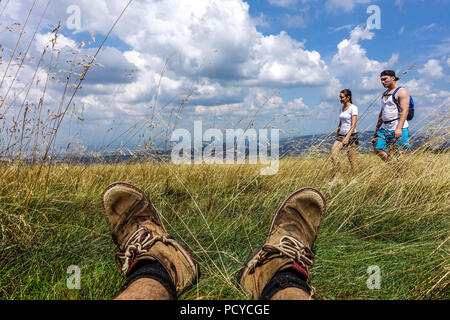 Wanderschuhe und Menschen, die auf einem Bergweg wandern, tschechische slowakische Grenze in Weißen Karpaten Blick auf die Stiefel und Füße eines Mannes, die im Gras ruhen Stockfoto