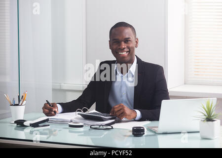 Happy afrikanischen Geschäftsmann auf der Suche nach Laptop Berechnung Rechnung im Büro Stockfoto