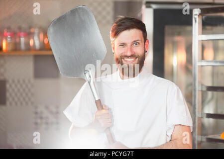 Eine junge lustig Bäcker mit pizza-Spachtel in der Hand vor dem Hintergrund der Backofen. Stockfoto