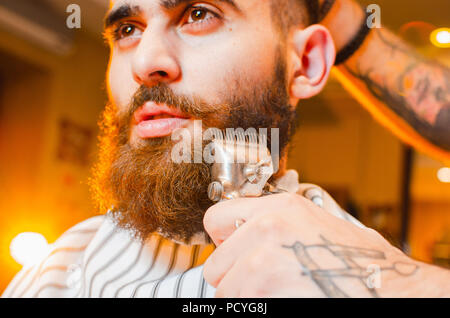 Friseur schneidet einen Bart von Vintage Haarschneidemaschinen, ein junger hübscher Kerl mit Bart und Schnurrbart. Herren Friseursalon. Stockfoto