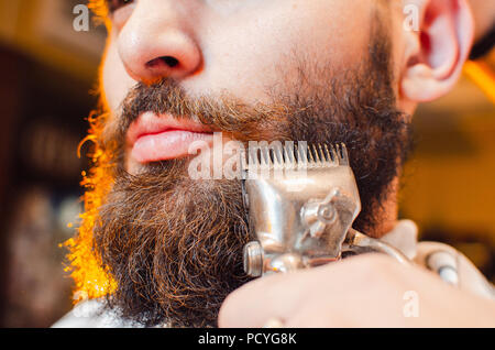 Friseur schneidet einen Bart von Vintage Haarschneidemaschinen, ein junger hübscher Kerl mit Bart und Schnurrbart. Herren Friseursalon. Stockfoto