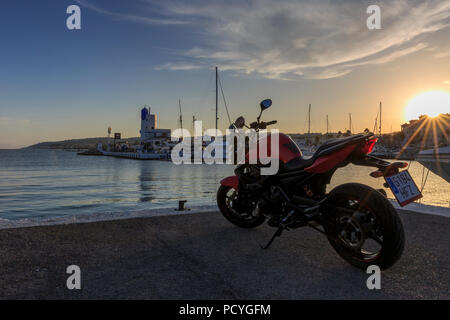 Ein rotes Motorrad steht am Kai an der kleinen Marina von Puerto de la Duquesa an der Costa del Sol, in der Nähe von Estepona, wie die Sonne untergeht Stockfoto