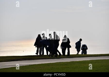 Eine Gruppe von Silhouette Menschen auf einen Weg mit Blick auf den Pazifischen Ozean auf einem trüben Tag. Stockfoto