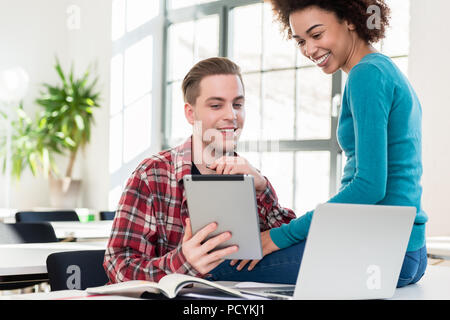 Zwei glückliche Schüler beobachten ein lustiges Video auf einem Tablet-PC Stockfoto
