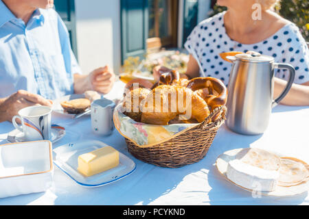 Zwei ältere Menschen mit Frühstück mit Brot Korb auf den Tisch im Sommer Garten Stockfoto