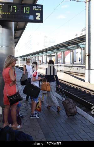 Frau orange Kleid und Junge, Warten, Zug auf Station Dnepr während ein Paar der Damen vorbei mit Taschen näher an der Stelle, wo die Schiene Auto stoppt zu erhalten Stockfoto