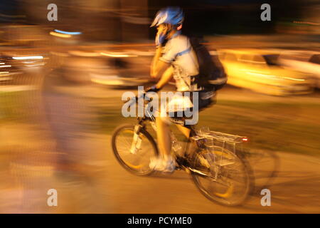 Radfahrer mit Sack, in Schutzhelm Pedale seiner Metall Pferd in Big City lights Gespräche auf seinem Weg Handy, holding Lenker mit einer Hand Stockfoto