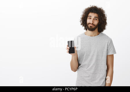 Innen- schuss der Ruhe casual attraktive männliche Kollegen in gestreiften T-Shirt, BlackBerry-Smartphone und lächelnd mit entspannter Freude Ausdruck, mit Stockfoto