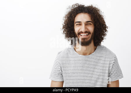 Taille-up Shot von freundlichen glücklich Hispanic bärtigen Mann mit lockigem Haar, trug stilvolle Gestreiftes T-Shirt, laut freudig Lachen, breit grinsend her Stockfoto