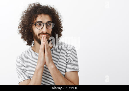 Wasit-up Shot von Stattlichen flirty bärtigen Mann mit lockigem Haar, beiseite und grinste, Brille mit gestreiften T-Shirt, Holding hands in Beten Stockfoto