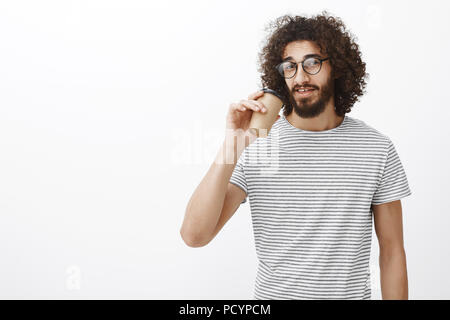 Portrait von zuversichtlich gut aussehende Slim männlichen Barista in trendigen t-shirt und Brillen, trinken Kaffee aus der Tasse und Blick auf die Kamera, in Pause und en Stockfoto