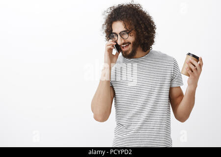 Studio shot zufrieden glücklich nach Freund mit lockigem Haar, Brille und stilvolle Gestreiftes T-Shirt, Tasse und gestikulierend während des Sprechens auf Stockfoto