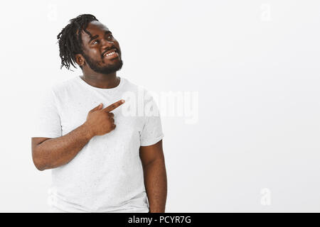 Studio geschossen von glücklich zufrieden attraktive dunkelhäutige Kerl in weißen T-Shirt, und zeigt in der oberen rechten Ecke, während das Lächeln von Zufriedenheit, Stockfoto