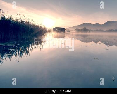 Romantischen sonnenaufgang Reflexion auf dem Kochelsee gegen Bootshäusern. Anfang Sommer morgen ansehen, Bayern, Deutschland Stockfoto