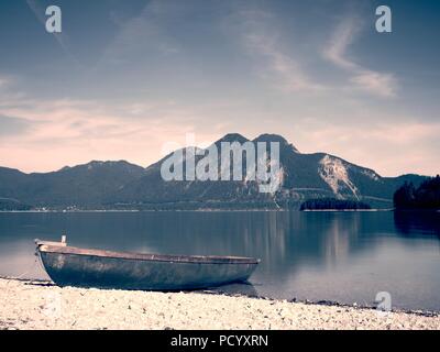 Boot auf dem steinigen Ufer eines Bergsees Walchensee. Warme Frühling Morgen mit Reflexion der Berge im grünen Wasser. Stockfoto