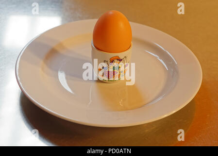 Ein gekochtes Ei in einer Little Miss Muffet Eierbecher auf einer weißen Platte warten, gegessen zu werden. Stockfoto