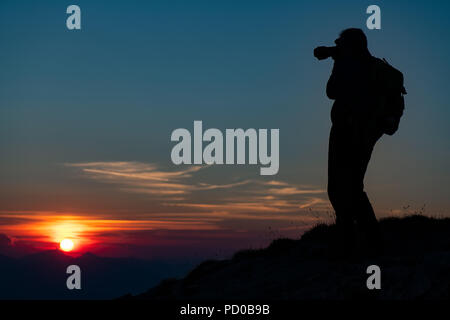 Fotografieren Sie den Sonnenuntergang in den Bergen. Fotograf in Silhouette. Stockfoto