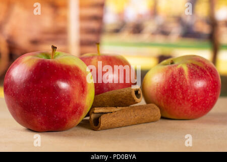Gruppe von drei ganzen frischen roten Apfel James Grieve Sorte mit Zimtstangen mit Karre im Hintergrund Stockfoto
