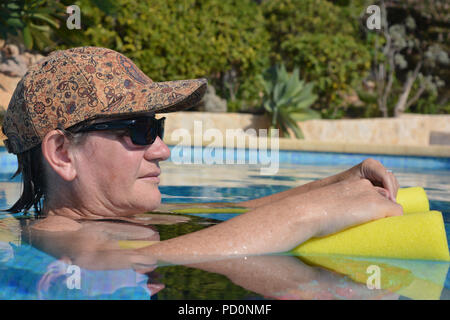 Frau trägt einen Hut und Sonnenbrille, schwimmend auf einem Pool Nudel in einem Schwimmbad, Profil anzeigen Stockfoto