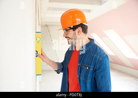 Lächelnd Heimwerker tragen, hart, Hut und legere Kleidung, während mit Wasserwaage auf die Bauunternehmen hat sich Website. Stockfoto