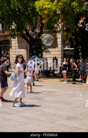 Kinder spielen mit Seifenblasen, die durch eine Straße Performer in der Plaza, Avinguda Catedral, 5, Barcelona, Spanien Stockfoto