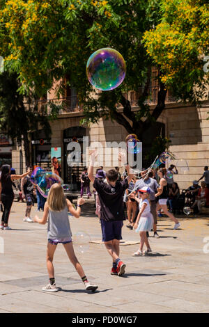 Kinder spielen mit Seifenblasen, die durch eine Straße Performer in der Plaza, Avinguda Catedral, 5, Barcelona, Spanien Stockfoto