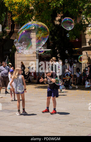 Kinder spielen mit Seifenblasen, die durch eine Straße Performer in der Plaza, Avinguda Catedral, 5, Barcelona, Spanien Stockfoto