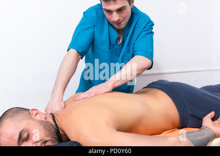 Masseur eine Rückenmassage auf einem männlichen Klienten in einer Klinik oder in Spa mit seinen Händen zu manipulieren und seine Muskeln in der Nähe zu 7/8 entspannen Stockfoto