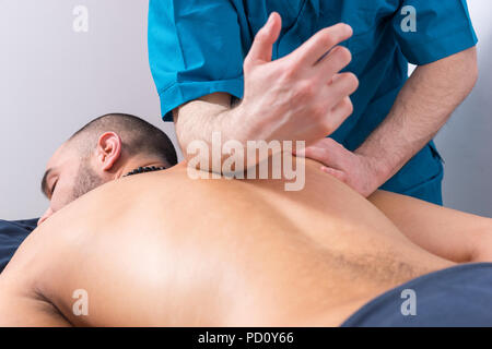 Professionelle masseur eine Wirbelsäule Massage auf einem männlichen Klienten Druck entlang der Wirbelsäule mit seinen Unterarm in der Nähe zu 7/8-Ansicht Stockfoto