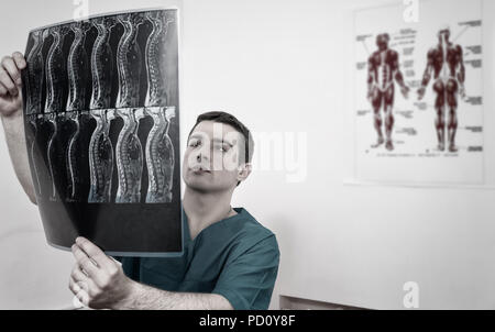 Getonten Bild von einem Arzt, der radiologe oder Physiotherapeuten die Prüfung eines x-ray von der Wirbelsäule halten Sie es gegen das Licht, mit anatomischer Charts hinter Stockfoto