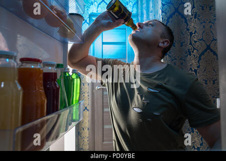 Durstigen es hinunter ein kaltes Bier, wie er in der offenen Tür von seinem Kühlschrank gesehen von innen heraus auf der Suche steht Stockfoto