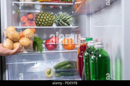Person, die Kunststoffbehälter mit frischem Gemüse aus dem offenen Kühlschrank Stockfoto