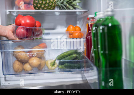 Person, die Kunststoffbehälter mit frischen Tomaten aus offenen Kühlschrank Stockfoto