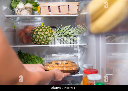 Person, die frischen Kuchen aus offenen Kühlschrank Stockfoto