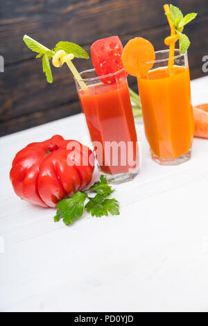 Hohe Gläser frisch zubereitete Tomaten und Orangensaft mit frischem Obst und Gemüse Zutaten neben in einem geneigten Winkel mit Kopie Raum Stockfoto