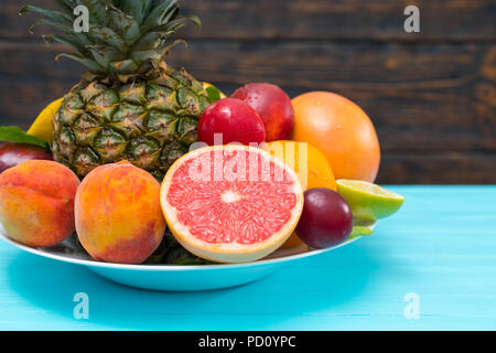 Rubinrote Grapefruit in Scheiben geschnitten auf einer Platte mit verschiedenen frischen Sommer tropische Früchte in der Nähe zu sehen, auf einem türkisblauen Tabelle Stockfoto