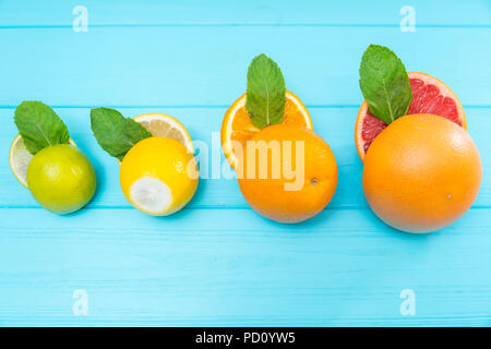 In Scheiben geschnitten halbiert sortierten frischer Zitrusfrüchte mit einer Limette, Zitrone, Orange und Pampelmuse auf einem türkis Holz Hintergrund mit Kopie Raum Stockfoto