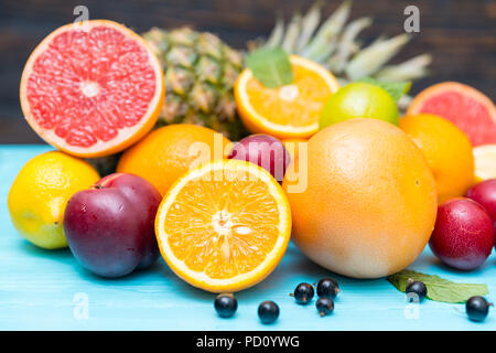 Frischen Zitrus- und Südfrüchte für eine gesunde Ernährung in einem Stapel auf einem blauen Holz Tisch mit verschiedenen Zitrusfrüchten, Pflaumen, Blaubeeren und Ananas angeordnet Stockfoto