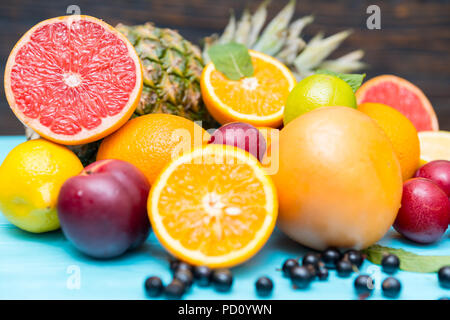 Sammlung von frischen tropischen Früchten für eine gesunde Ernährung mit einer Vielzahl von Zitrusfrüchten, Blaubeeren, Nektarinen, Pflaumen und Ananas in einem Stapel auf Blau Stockfoto