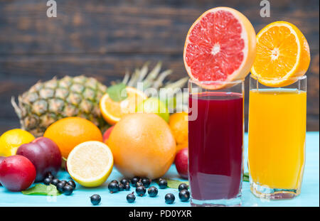 Gläser aus frisch gepresstem Fruchtsaft im Sommer mit einem von Orange und eine zweite von Blueberry mit Ruby Grapefruit garniert mit frischem Obst halbiert Stockfoto