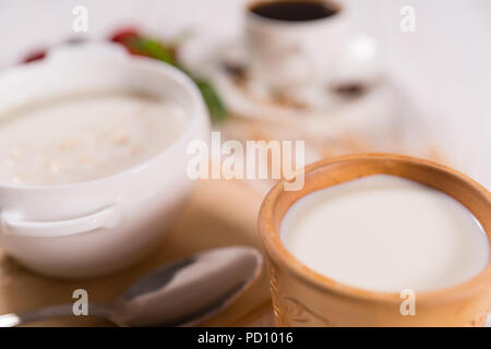 Schale oder kleine Kanne frische Milch, reich an Calcium auf ein Frühstückstisch mit einer unscharfen Schüssel Müsli und Kaffee im Hintergrund Stockfoto