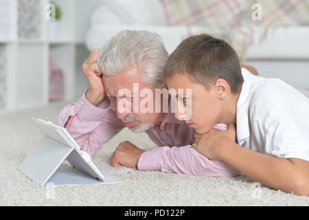 Großvater mit Enkel mit Tablette beim liegen auf dem Boden Stockfoto