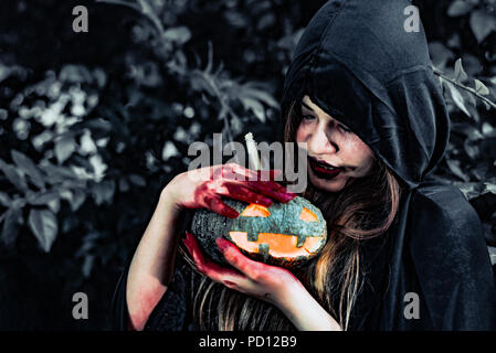 Daemon Hexe sorgen für Kürbis im Geheimnis Wald. Geist und Horror Konzept. Halloween Tag Thema. Rotes Blut auf Hexe Hände. Stockfoto