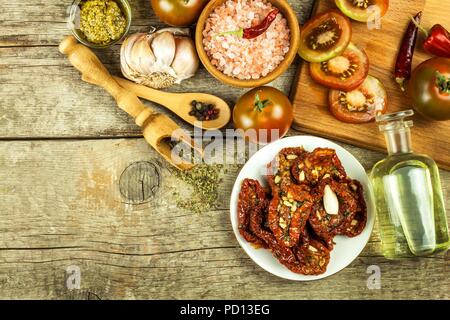 Getrocknete Tomaten mariniert in Olivenöl mit Knoblauch. Sonnenblumenkerne mit Tomaten auf einem alten Holztisch Stockfoto