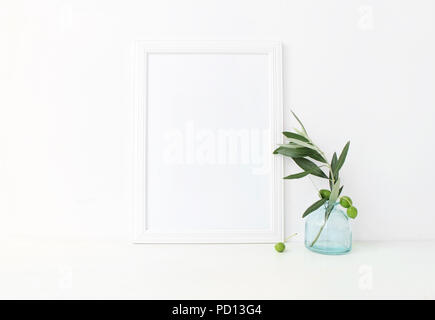 Weiße vertikale leer Holzrahmen mockup mit einem grünen Olivenzweigen in blauem Glas Vase auf dem Tisch liegen. Mediterrane Sommer poster Produkt Design. Styled lieferbar feminine Fotografie. Home Decor. Stockfoto
