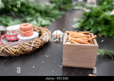 Box mit Zimtstangen und Dekor in den Vordergrund. Hersteller von Weihnachten Kranz aus Zweigen von Pinien für Urlaub. Master Class auf dem Bilden der dekorativen Ornamenten. Stockfoto