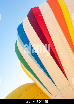 Zwei Heißluftballons wird aufgeblasen. Eine ist weiß mit blau, rot, orange, grün und gelb gestreift. Die andere ist gold gefärbt. Stockfoto