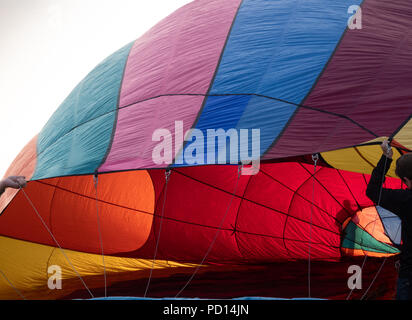 Zwei Menschen mit einem bunten Heißluftballon wie es mit Schatten im Hintergrund sichtbar ist eine dritte Person aufgeblasen wird. Stockfoto